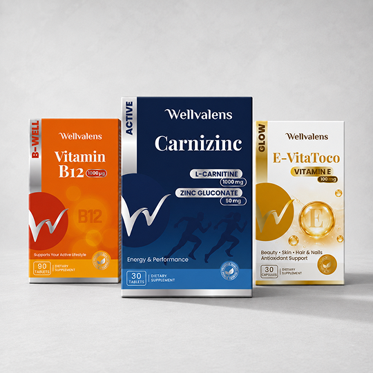 Three Wellvalens dietary supplement boxes arranged together on a light gray studio background: an orange Vitamin B12 box on the left, a dark blue Carnizine box in the center, and a white E-VitaToco Vitamin E box on the right.