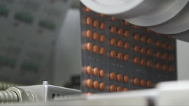 Orange tablets sealed in a blister pack strip passing through a packaging machine