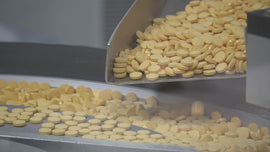 Yellow round tablets pouring from a metal chute onto a conveyor in a production line