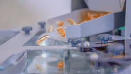 Translucent orange softgel capsules sliding down a metal chute on an automated production line