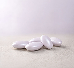 Five smooth, glossy white oval candies or pills arranged on a light beige surface against a soft light gray background.